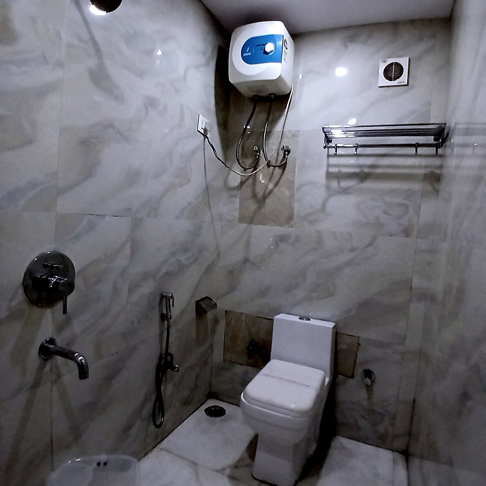A marble-tiled attached bathroom with a shower and geyser