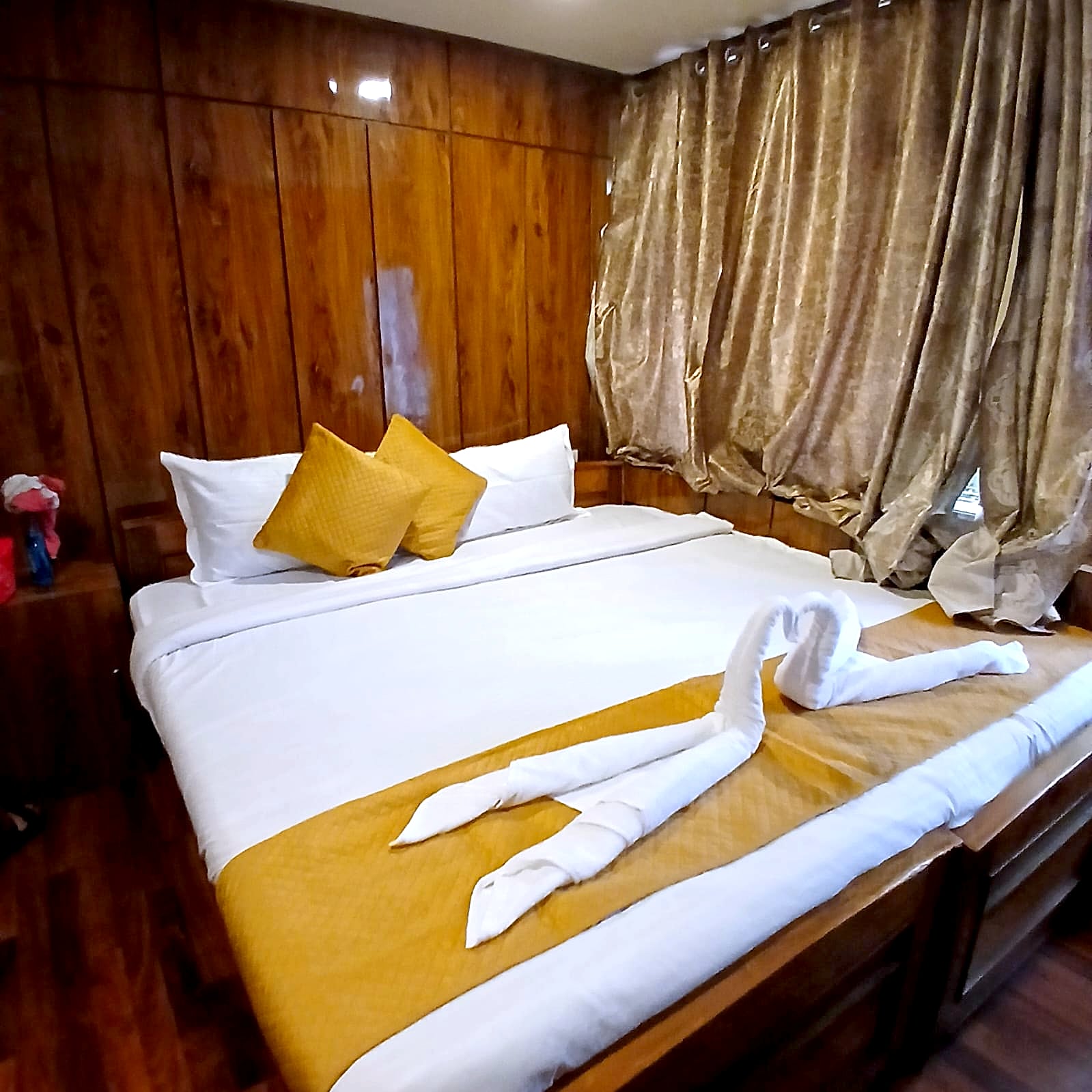 A double room at Hotel Charlie with a gold runner on the bed and curtained windows